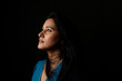© abir - Close up face portrait of a beautiful Indian Bengali brunette woman in light and shadow before a black copy space background wearing a blue top. Indian lifestyle and fashion  portrait