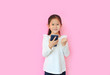 © zilvergolf - Happy asian little child girl watching her smartphone and expression hand fight sign over pink background. Kid smiling and enjoy while playing cellphone.