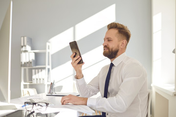 Wall Mural - Serious busy businessman reads message on the phone at a table with a computer in the office.