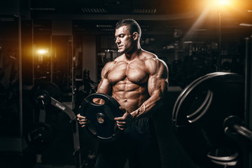 Wall Mural - Muscular man bodybuilder training in gym and posing. Fit muscle guy workout with weights and barbell
