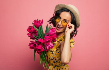 The portrait of a happy excited gorgeous young woman in stylish wear is posing with a freshness bunch of tulips. Mothers day. Women's holidays. Springtime.