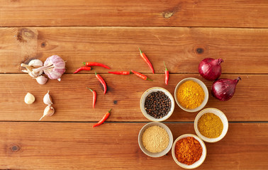 food, culinary and eating concept - bowls with different spices, onion, garlic and red hot chili peppers on wooden table