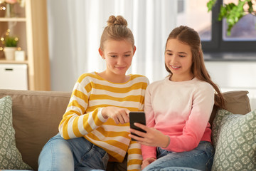 Wall Mural - people, technology and friendship concept - happy teenage girls with smartphone sitting on sofa at home