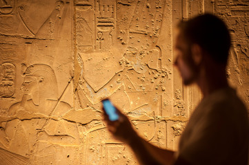 Wall Mural - unrecognizable tourist standing using smartphone in front of an illuminated panel of hieroglyphics i