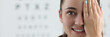 Leinwandbild Motiv Portrait of lady oculist smiling and looking at camera with happiness. Cheerful doctor standing in clinic office and covering left eye with tender hand. Vision test concept