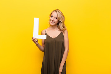 Wall Mural - young blonde woman excited, happy, joyful, holding the letter L of the alphabet to form a word or a sentence.