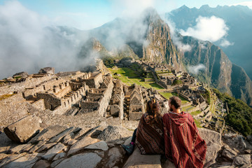 Couple dressed in ponchos watching the ruins of Machu Picchu