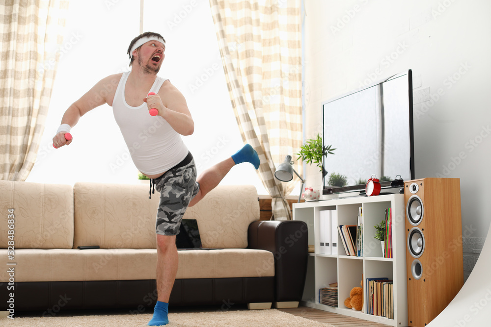 Young handsome man in shorts and vest holds pink dumbbells in hand. Watch tv lessons single combats is practicing receptions of sensei one home fitness indoor training independent education remotely - obrazy, fototapety, plakaty 