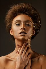 Wall Mural - Fashion art portrait of model girl with holiday golden shiny professional makeup. beaty woman with golden sparkles on skin and hair on dark background. Gold glowing skin.