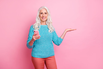 Wall Mural - Portrait of positive cheerful old woman promoter use smartphone hold hand recommend online product ads promotion wear casual style sweater isolated over pastel color background