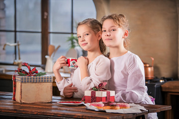 Two girls near the table drink tea, hug and watch gifts