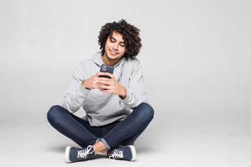 young curly man sitting on the floor sending a message isolated on white background