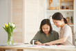 © AnnaStills - Horizontal shot of two Asian sisters sitting together at table indoors making cards for Mother's Day