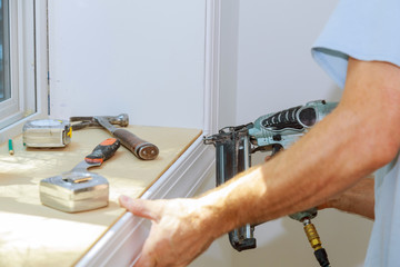 Wall Mural - Carpenter using air nail gun to moldings for window