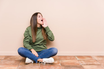 Wall Mural - Young caucasian woman sitting on the floor isolated shouting and holding palm near opened mouth.