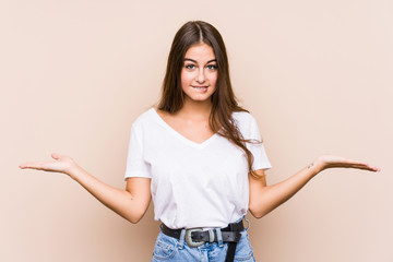 Wall Mural - Young caucasian woman posing isolated confused and doubtful shrugging shoulders to hold a copy space.