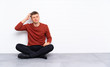 © luismolinero - Young handsome man sitting on the floor having doubts and with confuse face expression