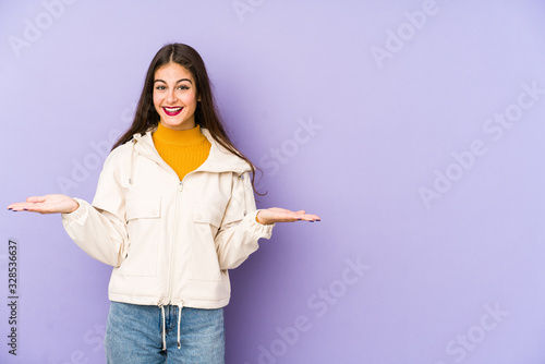 Fotografía Young caucasian woman isolated on purple background makes scale with arms, feels happy and confident