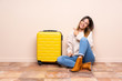 © luismolinero - Traveler woman with suitcase sitting on the floor celebrating a victory