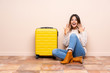 © luismolinero - Traveler woman with suitcase sitting on the floor with surprise facial expression