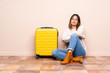 © luismolinero - Traveler woman with suitcase sitting on the floor keeping arms crossed