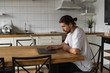© Volodymyr_sh - Freelancer working from home on the kitchen and using laptop. Bearded man working with a laptop and reading good news. Handsome successful self entrepreneur sitting and working at his modern home.