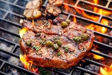 Wall Mural - Grilled pork steak pork neck  with addition of capers and aromatic herbs on the grill plate, close up. 