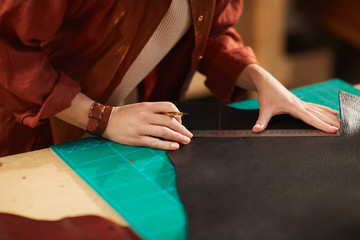 Wall Mural - Unrecognizable female artisan measuring piece of dark brown leather to cut it out, horizontal shot