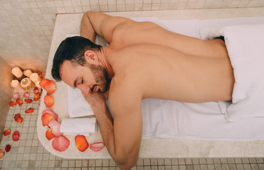 Caucasian man in romantic setting enjoys relaxing in Turkish bath. Hot marble table warms a man's body in a hammam