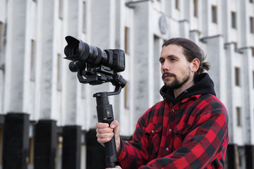 Young Professional videographer holding professional camera on 3-axis gimbal stabilizer. Pro equipment helps to make high quality video without shaking. Cameraman wearing red shirt making a videos.