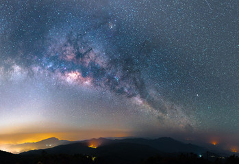 the panorama of arching milky way galactic center over the mountain with city light.