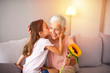© Dragana Gordic - Cute girl giving a bunch of flowers to her grandmother sitting on the couch. Happy grandmother hugging small cute grandchild thanking for flowers presented. Darling granddaughter always remembers