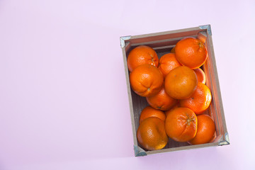 lot of tangerines in a wooden box on a pink background