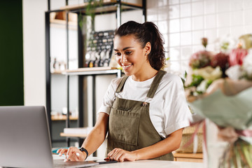 Wall Mural - Young shop owner using a laptop. Florist woman standing at counter.