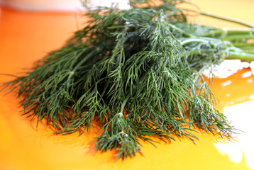 A bunch of dill on an orange table. Veggie food. Greens on a glossy table.