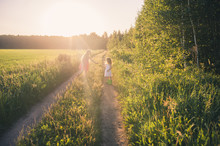 Two Cute Girls Walking On A Country Road In A Field At Sunset