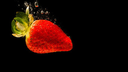 Wall Mural - Strawberry falling into water causing bubbles all around it. Healthy food concept