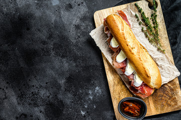 Wall Mural - baguette sandwich with jamon ham serrano, paleta iberica, Camembert cheese on the cutting Board.  Black background, top view, space for text