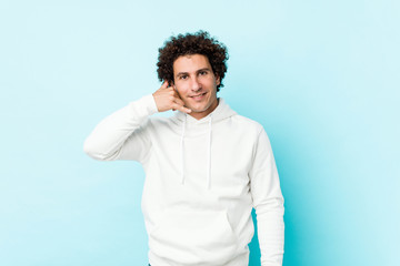 Young sporty man against a blue background showing a mobile phone call gesture with fingers.