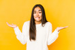 Young woman isolated on a yellow background confused and doubtful shrugging shoulders to hold a copy space.