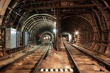 Two Railway Lines Are Laid Next To Each Other. The Railway Line Turns To The Left, The Railway Line Runs Straight. A Brightly Illuminated Tunnel With Reinforced Concrete Walls. Electric Cables.
