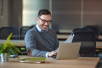 Crop side view of adult male worker in formal shirt and glasses sitting at desk with documents and working on person computer with empty white screen in workplace.