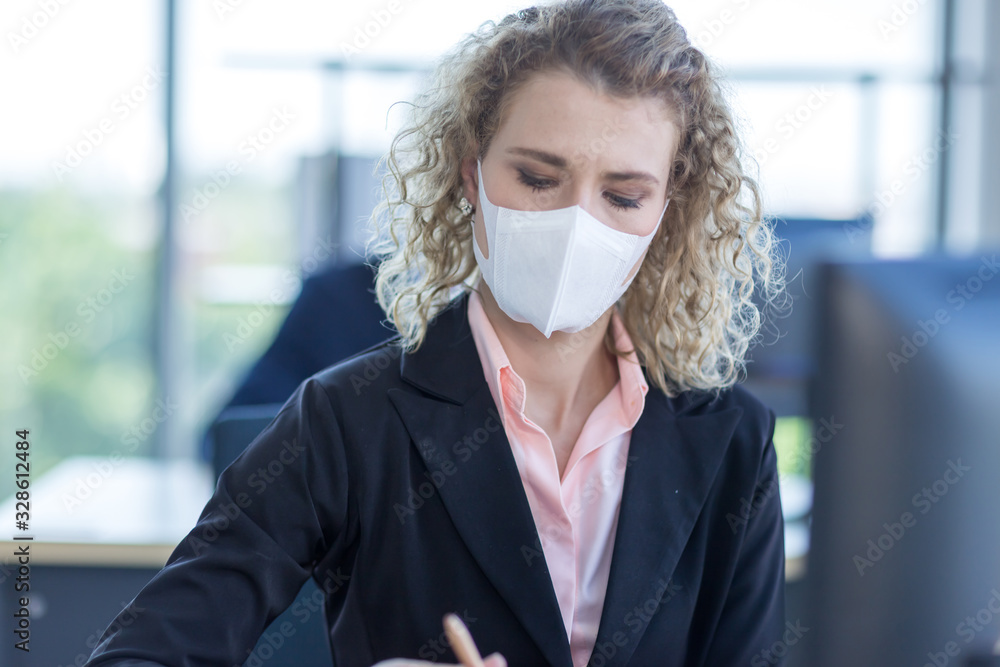 Business woman with curly blonde hair wearing a mask sitting in office ...