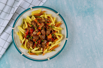 Penne pasta with beef stew with vegetable in plate on blue table.