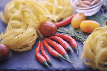 Pasta on the table with spices and vegetables. Noodles with vegetables for cooking on a black stone background.