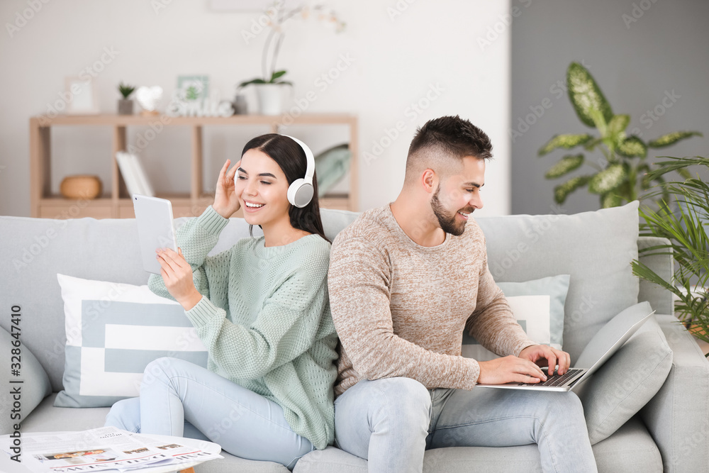 Young couple with modern devices resting on sofa at home