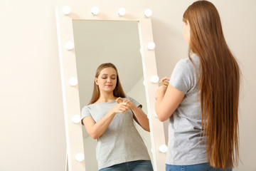 Sticker - Beautiful young woman applying face serum in front of mirror at home