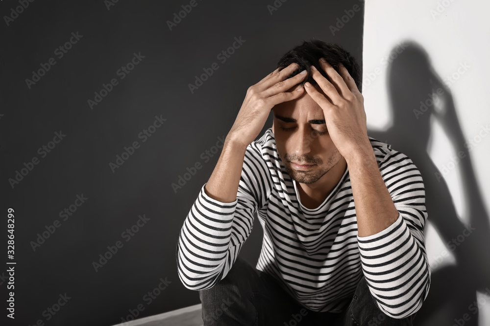 Depressed young man sitting near wall