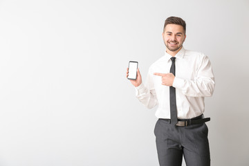 Wall Mural - Young businessman with mobile phone on light background