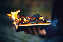 The Sorcerer's Hand Holds A Thick Hardcover Magic Book That Burns With A Bright Fire In The Middle Of The Night And Emits Sparks And Ashes Into The Air.